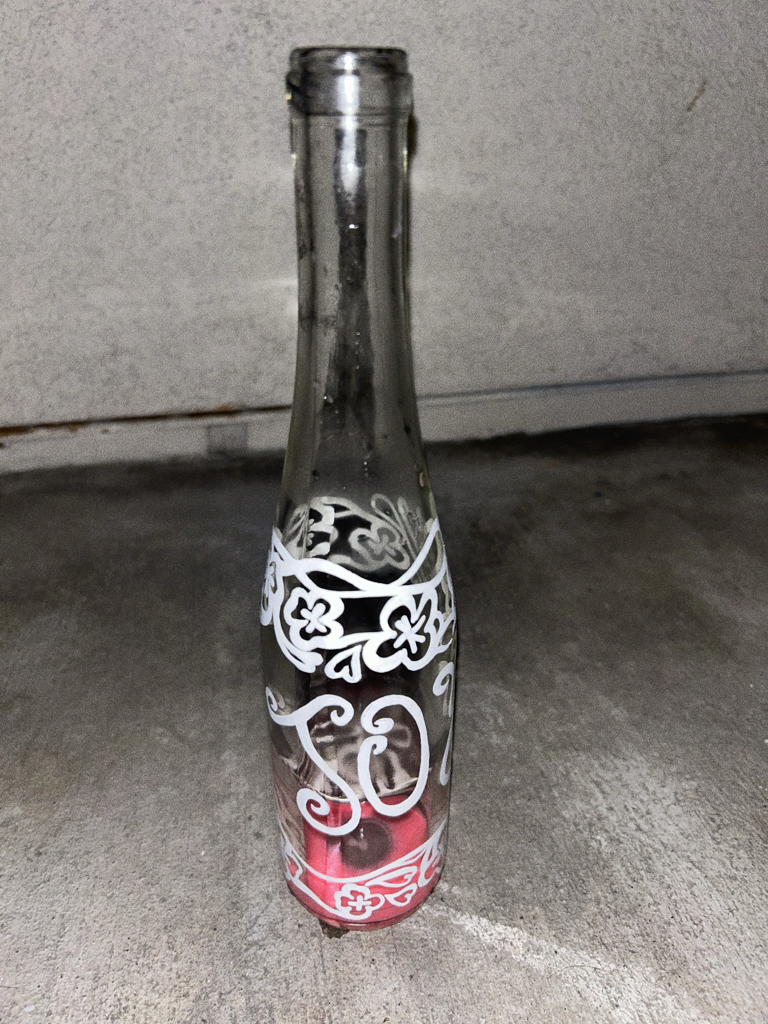 The same bottle, now emptied, photographed against a concrete floor and garage door.